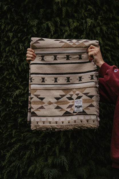 Person holding a patterned blanket against a dark green hedge