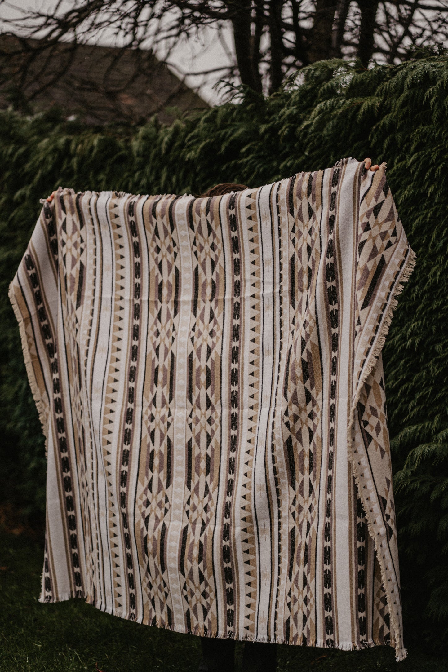 Person holding a patterned blanket against a hedge