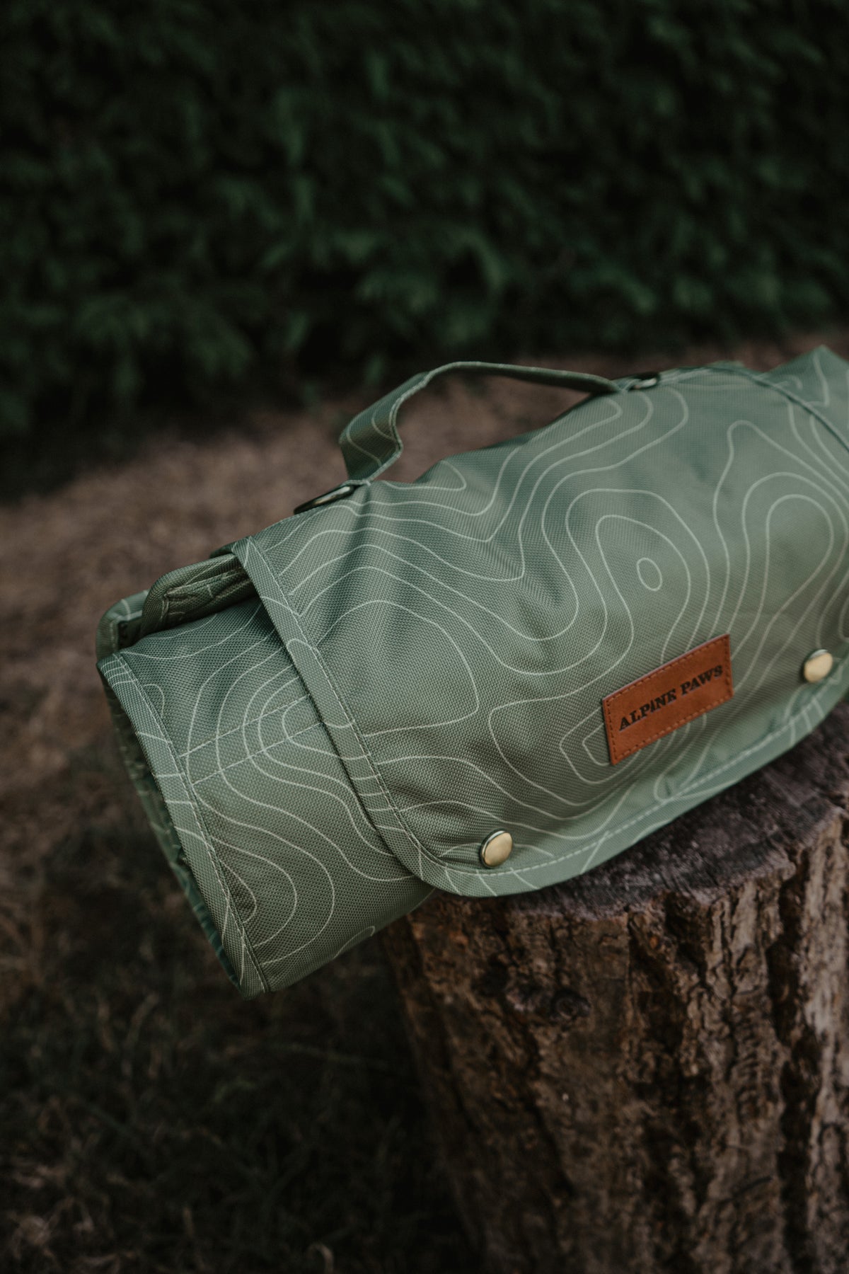 A green travel mat with a white topographic contour line pattern, resting on a tree stump outdoors. 