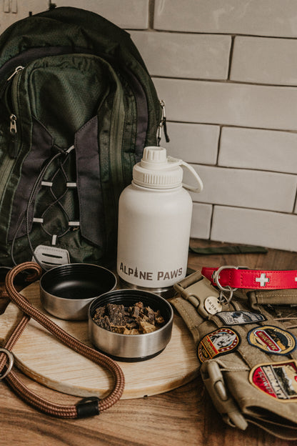 Outdoor adventure gear including a backpack, travel dog water bottle, and dog supplies on a wooden surface.