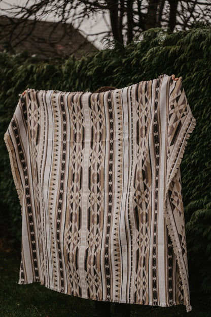 Person holding a patterned woven beige blanket against a hedge