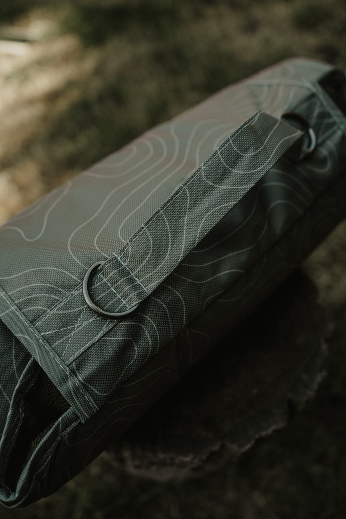 A close-up of a green topographic-patterned dog mat resting on a dark textured surface with a blurred outdoor background.